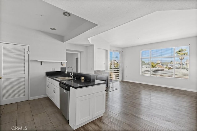 kitchen featuring baseboards, dishwasher, a sink, dark countertops, and a peninsula
