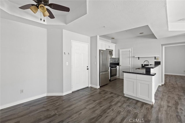 kitchen featuring a raised ceiling, a sink, dark countertops, appliances with stainless steel finishes, and white cabinetry
