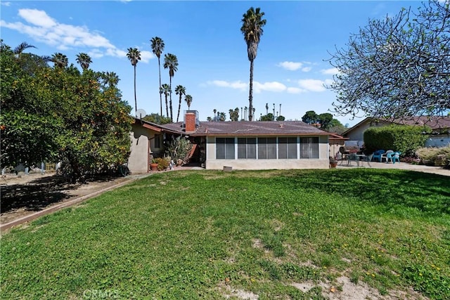 back of house with a sunroom, a patio, a chimney, stucco siding, and a lawn