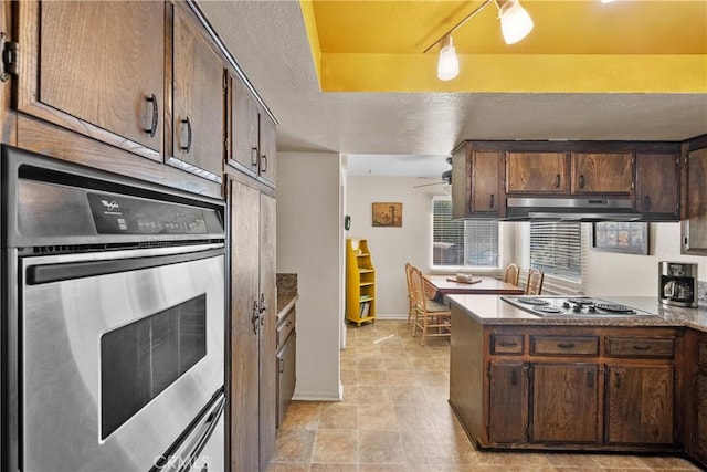 kitchen featuring stainless steel appliances, under cabinet range hood, a textured ceiling, a peninsula, and dark brown cabinetry