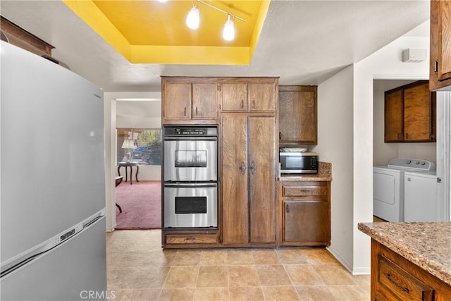 kitchen featuring independent washer and dryer, baseboards, brown cabinets, stainless steel appliances, and a raised ceiling