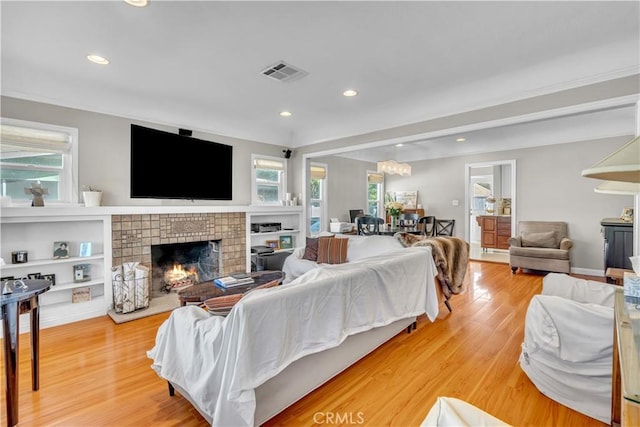 living area with a lit fireplace, light wood-type flooring, visible vents, and recessed lighting