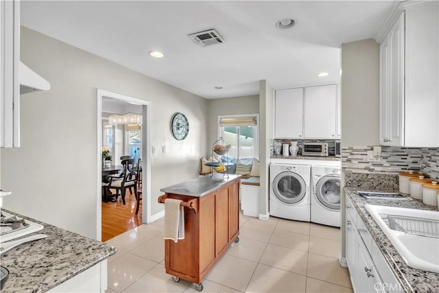 washroom featuring light tile patterned floors, visible vents, separate washer and dryer, a sink, and laundry area