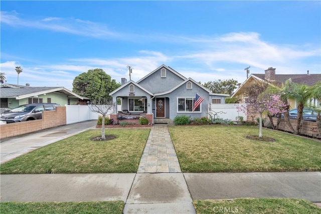 bungalow-style house with a front yard, driveway, stucco siding, and fence