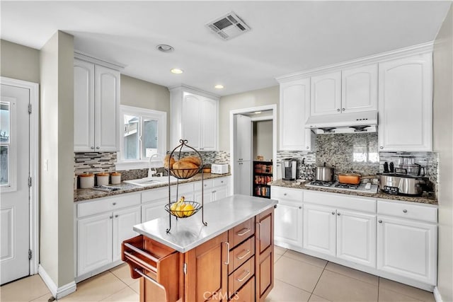 kitchen with light tile patterned flooring, under cabinet range hood, visible vents, stainless steel gas cooktop, and a sink