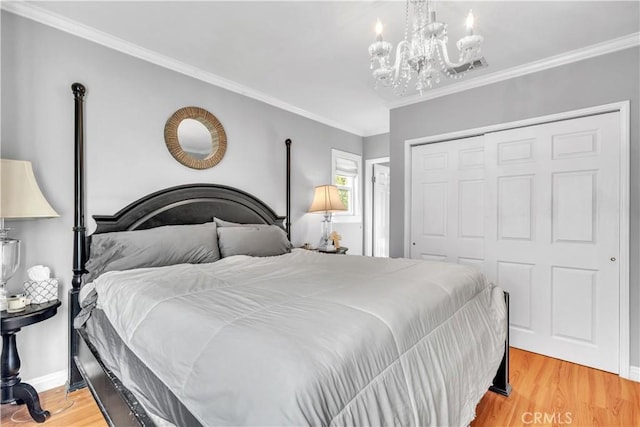 bedroom with light wood-type flooring, a closet, ornamental molding, a notable chandelier, and baseboards