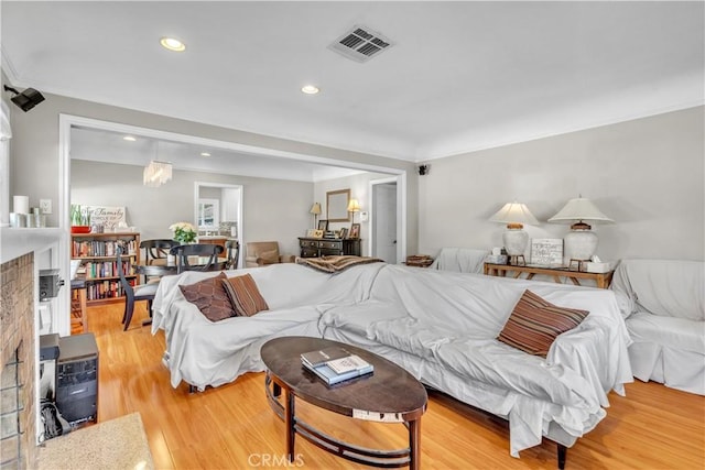 living room with a fireplace, ornamental molding, visible vents, recessed lighting, and light wood finished floors