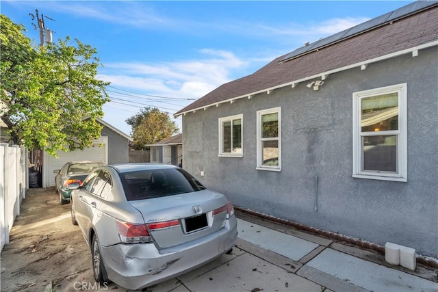 view of property exterior with roof with shingles, stucco siding, an outdoor structure, and fence