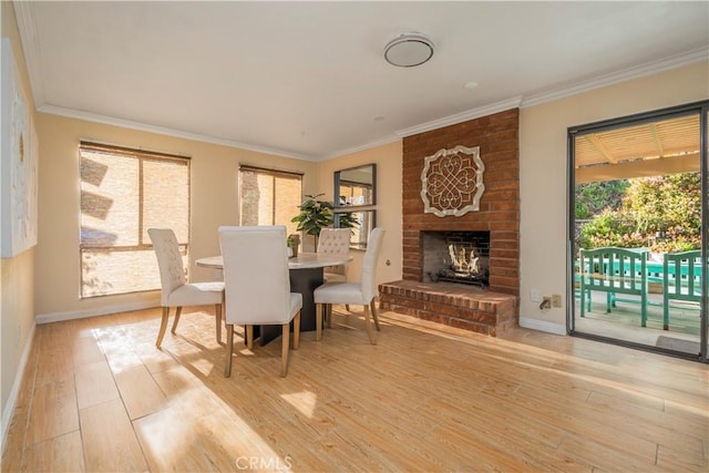 dining room featuring a brick fireplace, baseboards, light wood-style floors, and crown molding