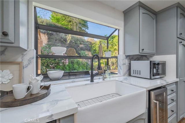 kitchen featuring tasteful backsplash, beverage cooler, a sink, and gray cabinetry