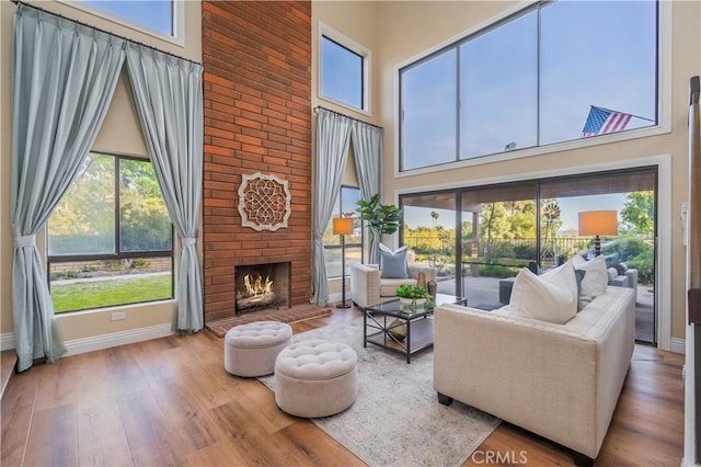 living area featuring a brick fireplace, a healthy amount of sunlight, a towering ceiling, and baseboards