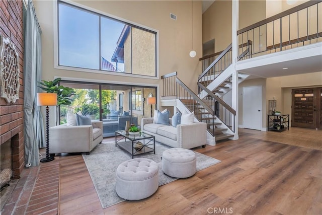 living room with visible vents, a towering ceiling, wood finished floors, stairs, and a fireplace