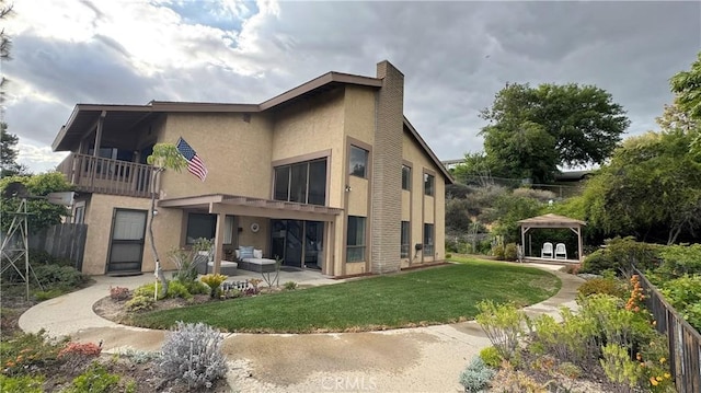 back of house featuring a gazebo, a patio area, a lawn, a balcony, and stucco siding