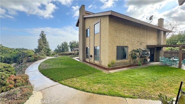 view of property exterior featuring a chimney, fence, stucco siding, a patio, and a lawn