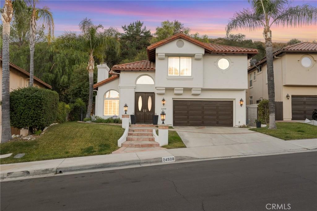 24508 Ebelden Ave, Newhall, CA 91321 - mediterranean / spanish house featuring concrete driveway, stucco siding, an attached garage, a tiled roof, and a lawn