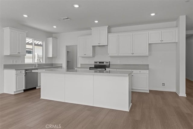 kitchen featuring a center island, a sink, white cabinetry, wood finished floors, and stainless steel appliances