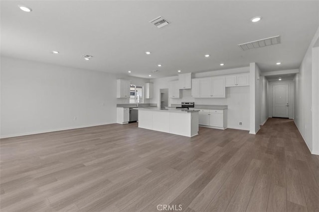 kitchen featuring visible vents, white cabinets, open floor plan, light wood-style flooring, and a kitchen island