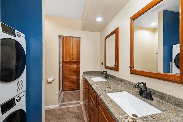 full bath with a sink, baseboards, tile patterned flooring, and stacked washer and clothes dryer