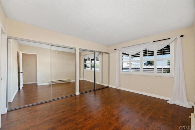 unfurnished bedroom with wood finished floors, two closets, baseboards, baseboard heating, and a textured ceiling