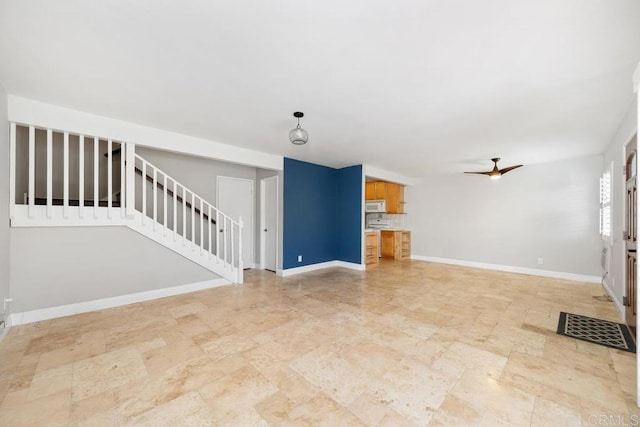 unfurnished living room featuring baseboards, stairs, ceiling fan, and stone finish floor