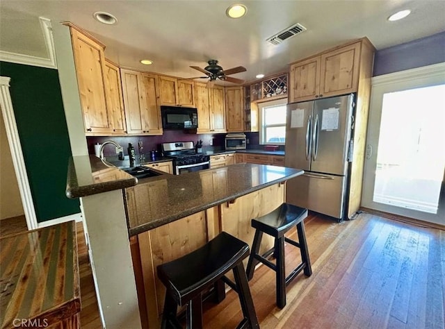 kitchen with a peninsula, a sink, visible vents, a breakfast bar, and appliances with stainless steel finishes