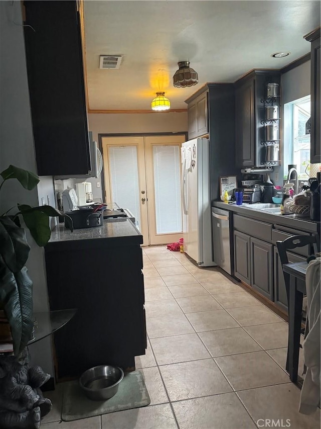 kitchen with stainless steel dishwasher, a sink, light tile patterned floors, visible vents, and freestanding refrigerator