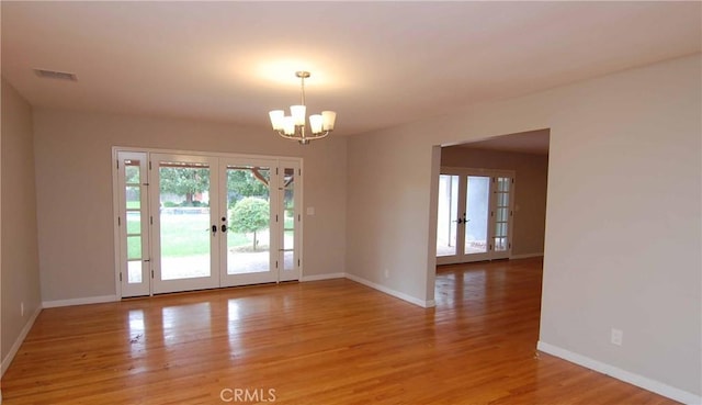 spare room featuring french doors, light wood-style flooring, and an inviting chandelier
