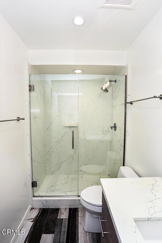 bathroom with vanity, toilet, a marble finish shower, recessed lighting, and wood finished floors