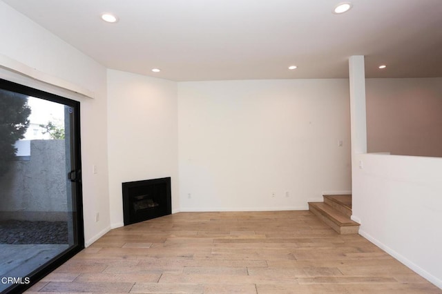 unfurnished living room with a fireplace, recessed lighting, baseboards, light wood-type flooring, and stairway