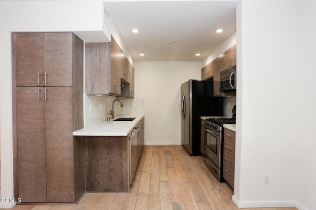 kitchen featuring recessed lighting, light countertops, a sink, light wood finished floors, and appliances with stainless steel finishes