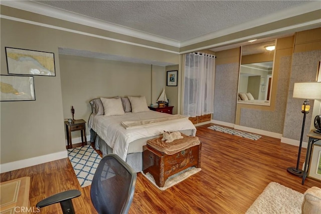 bedroom featuring baseboards, ornamental molding, a textured ceiling, and wood finished floors