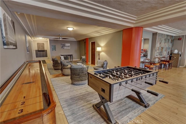 recreation room featuring a raised ceiling, ornamental molding, a textured ceiling, and wood finished floors