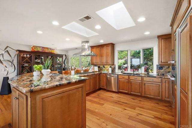 kitchen featuring brown cabinetry, island range hood, appliances with stainless steel finishes, and a skylight