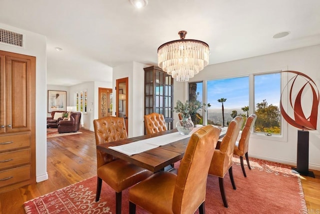 dining space featuring baseboards, a chandelier, visible vents, and wood finished floors