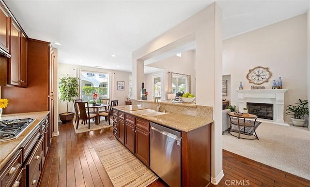 kitchen featuring dark wood-style flooring, a glass covered fireplace, open floor plan, a sink, and appliances with stainless steel finishes