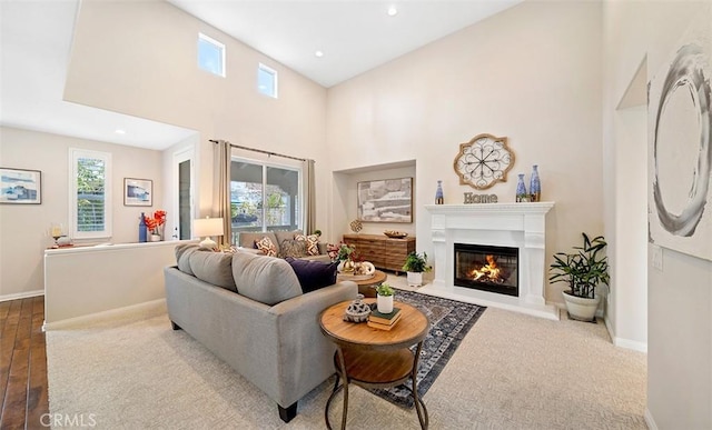 living area featuring baseboards, recessed lighting, a glass covered fireplace, and a high ceiling