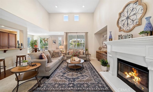 living room with a glass covered fireplace, a towering ceiling, baseboards, and a healthy amount of sunlight