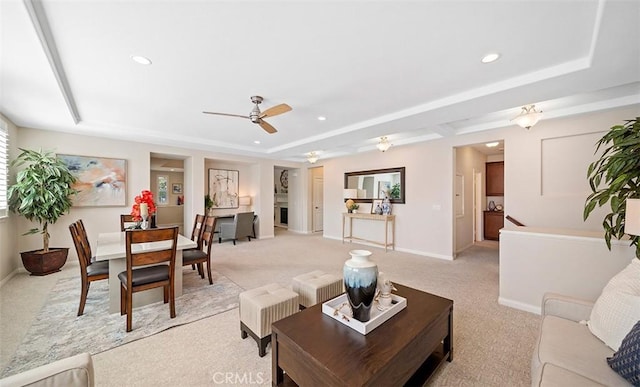 living area featuring a tray ceiling, light carpet, and ceiling fan