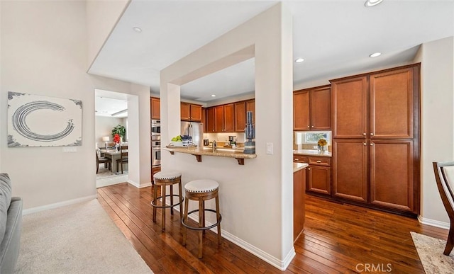 kitchen featuring recessed lighting, dark wood-style flooring, brown cabinets, and a kitchen bar