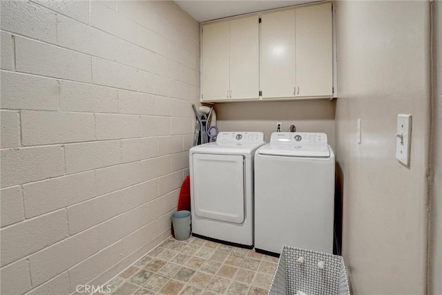 clothes washing area featuring cabinet space, concrete block wall, and washer and dryer