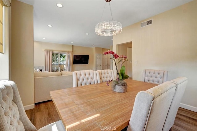 dining area with baseboards, a notable chandelier, wood finished floors, and visible vents