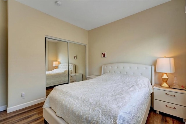 bedroom with dark wood-type flooring, baseboards, and a closet