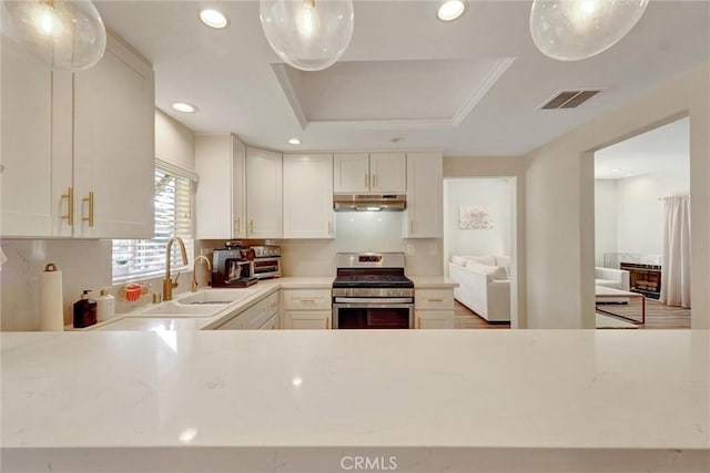 kitchen with visible vents, a raised ceiling, under cabinet range hood, stainless steel range with gas stovetop, and a sink