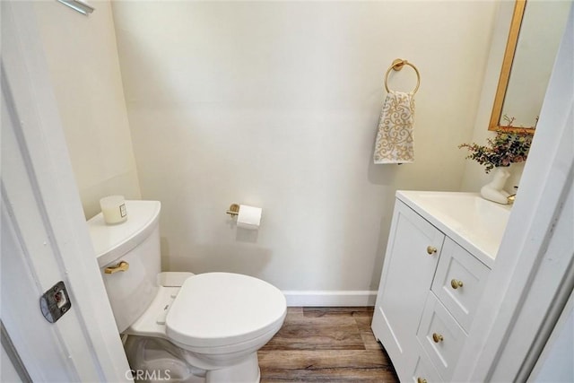 half bathroom with baseboards, wood finished floors, toilet, and vanity