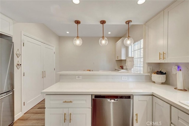 kitchen featuring a peninsula, light countertops, white cabinets, light wood finished floors, and stainless steel appliances