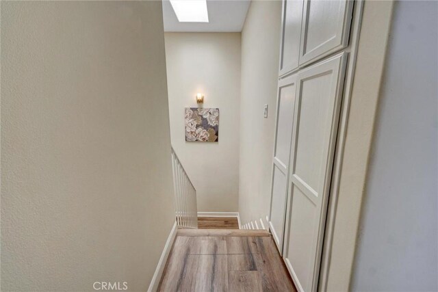 corridor with baseboards, a skylight, and wood finished floors