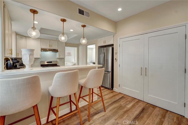 kitchen with visible vents, stainless steel appliances, light wood finished floors, a peninsula, and under cabinet range hood