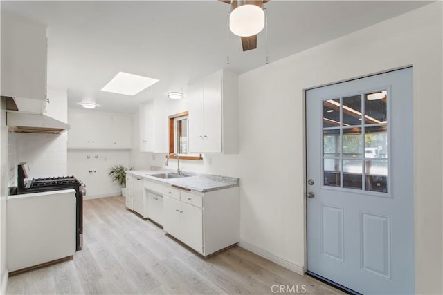 kitchen featuring exhaust hood, light wood-style flooring, a skylight, gas range, and a sink