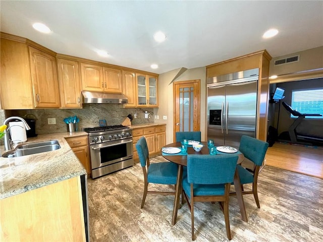 kitchen with visible vents, under cabinet range hood, a sink, light wood finished floors, and appliances with stainless steel finishes