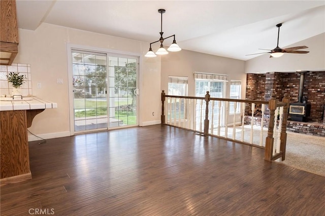 interior space featuring lofted ceiling, a wood stove, baseboards, dark wood-type flooring, and a ceiling fan